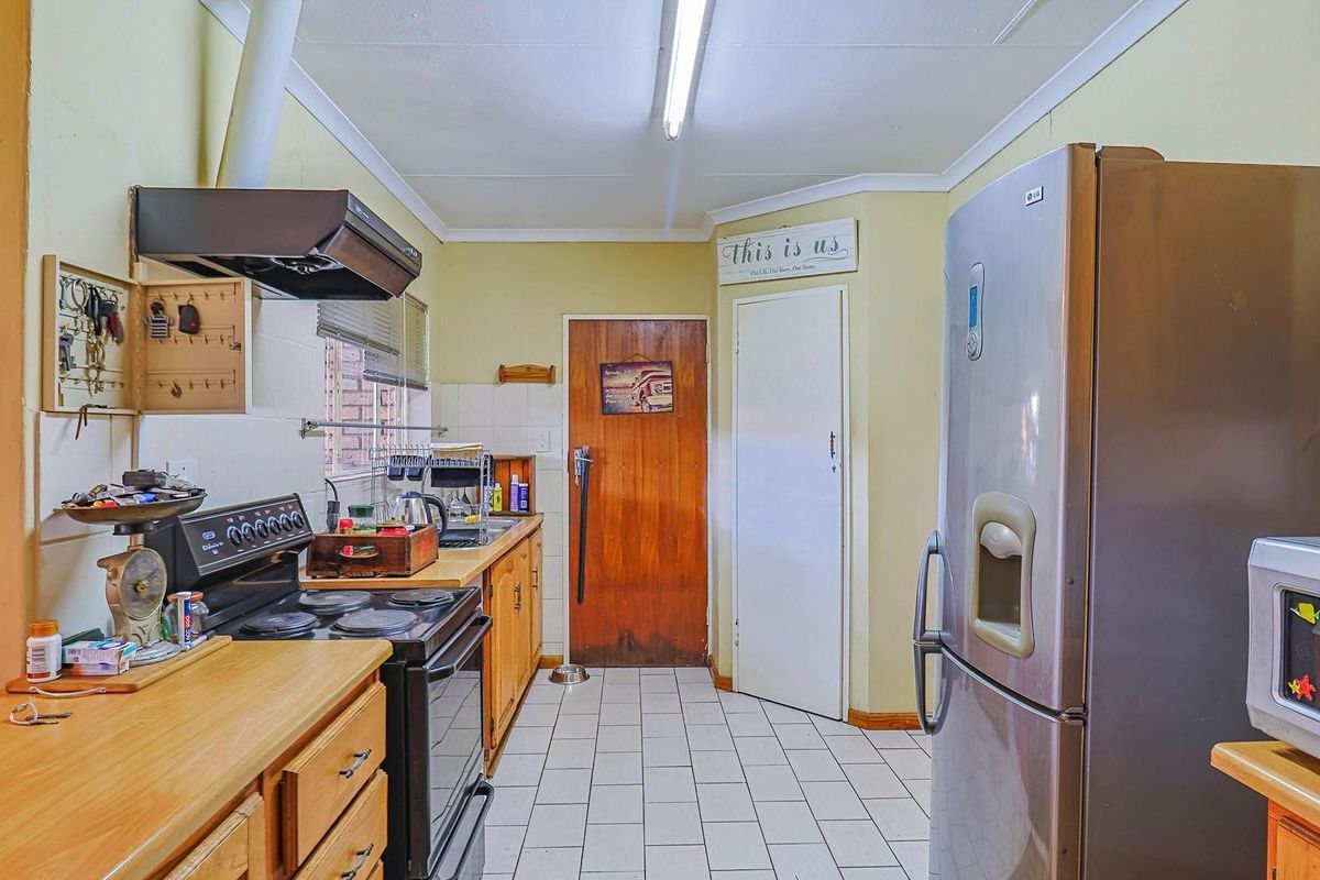 A functional kitchen featuring wooden cabinetry, tiled flooring, a built-in extractor fan, and direct access to adjacent rooms.