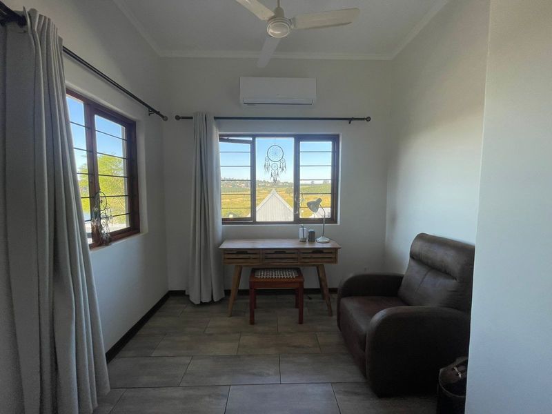 A bright bedroom featuring tiled flooring, a ceiling fan, and a wall-mounted air conditioning unit, with large windows offering natural light and exterior views.