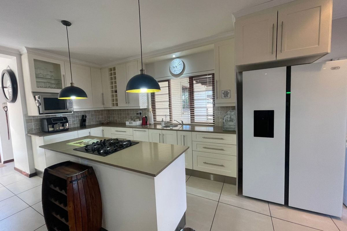 Modern kitchen featuring light-toned cabinetry, stone countertops, a central island with a gas hob, and integrated appliances, finished with neutral floor tiles.