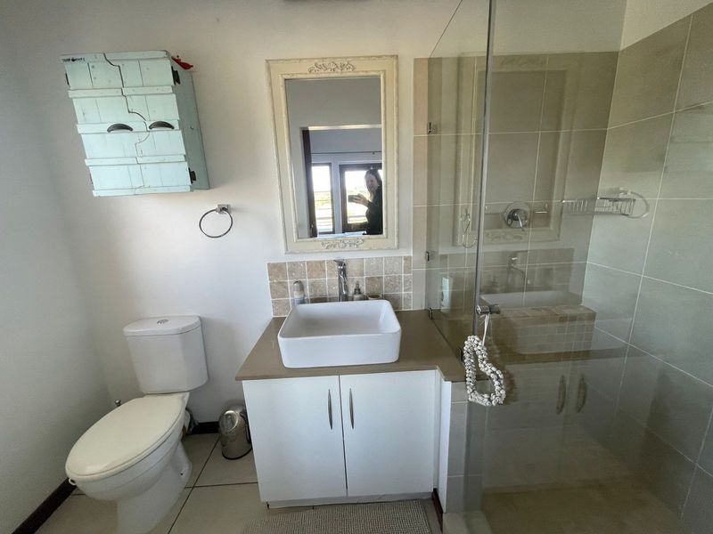 A functional bathroom featuring a vessel sink vanity, glass-enclosed shower, and neutral wall tiling.
