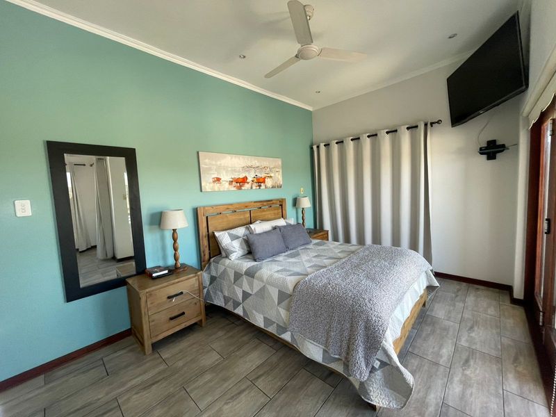 A well-maintained bedroom featuring tiled flooring, a ceiling fan, and recessed lighting, with a feature wall and direct access to an outdoor area.