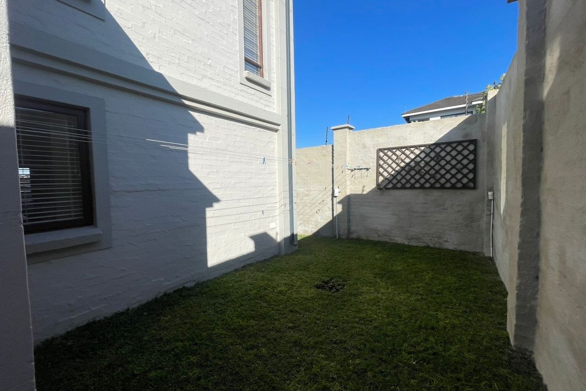 A private rear courtyard featuring a small lawn area, painted brick exterior walls, and a boundary wall with a decorative trellis.
