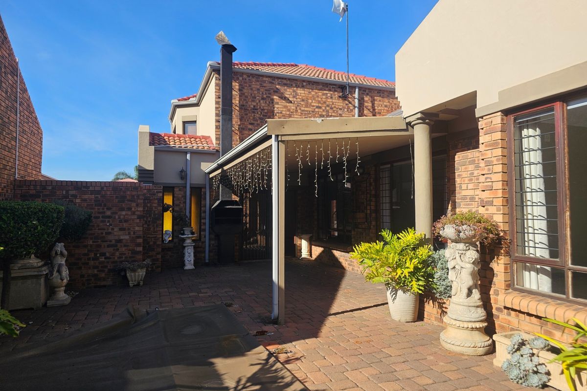 A paved rear patio area featuring a built-in braai, covered entertainment space, and brick wall perimeter, ideal for outdoor dining and relaxation.