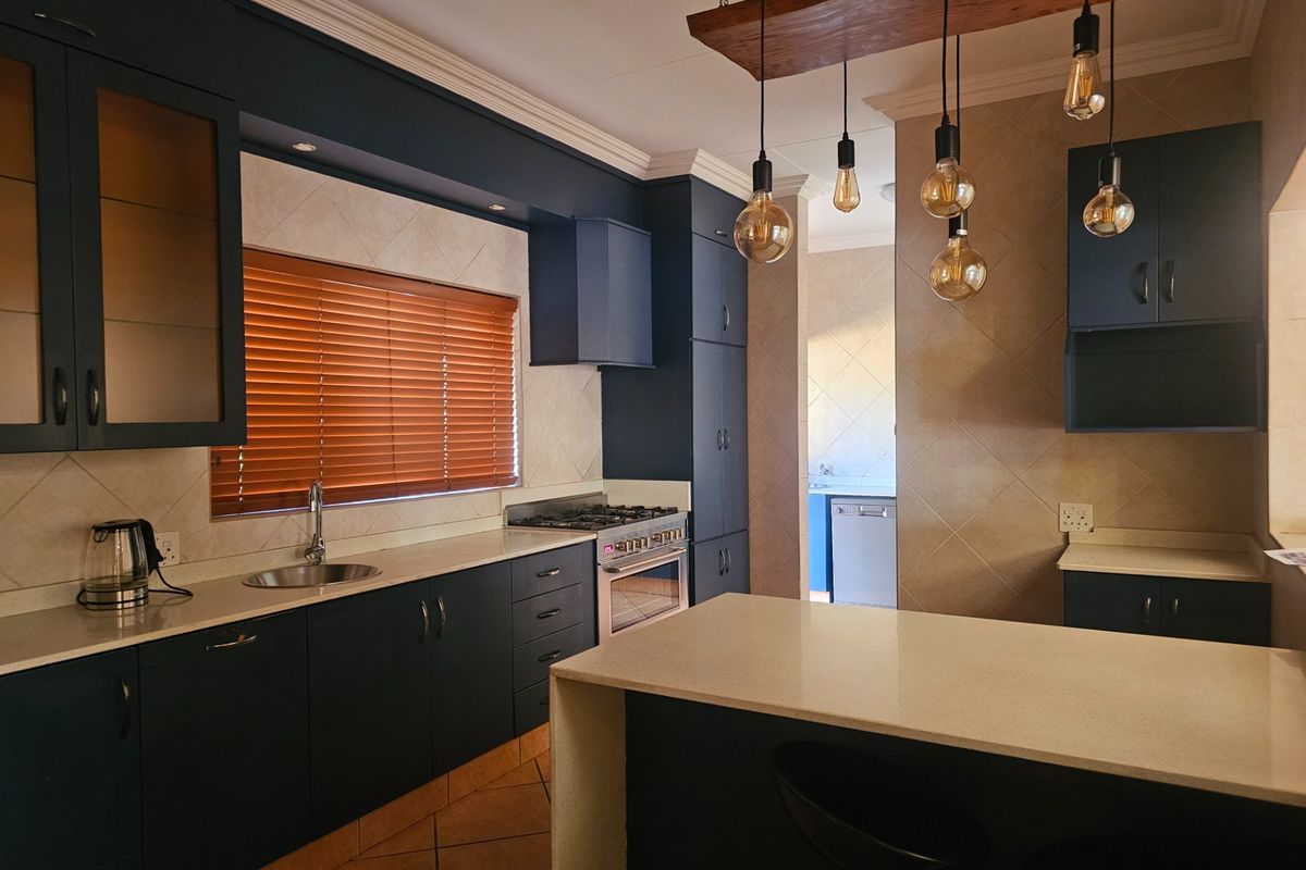Modern kitchen featuring dark cabinetry, stone countertops, a built-in gas stove, and a central island with pendant lighting, leading into a scullery area.