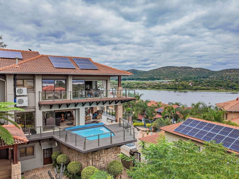 Elevated rear view of a multi-story residence featuring solar panels, a raised swimming pool, expansive balconies, and scenic waterfront views.