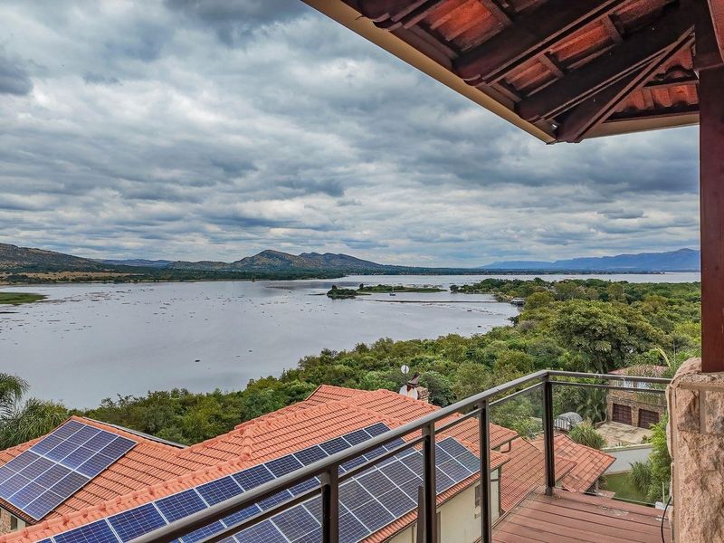 Elevated balcony view overlooking a large lake and surrounding landscape, featuring a covered patio area with stone and timber architectural details.