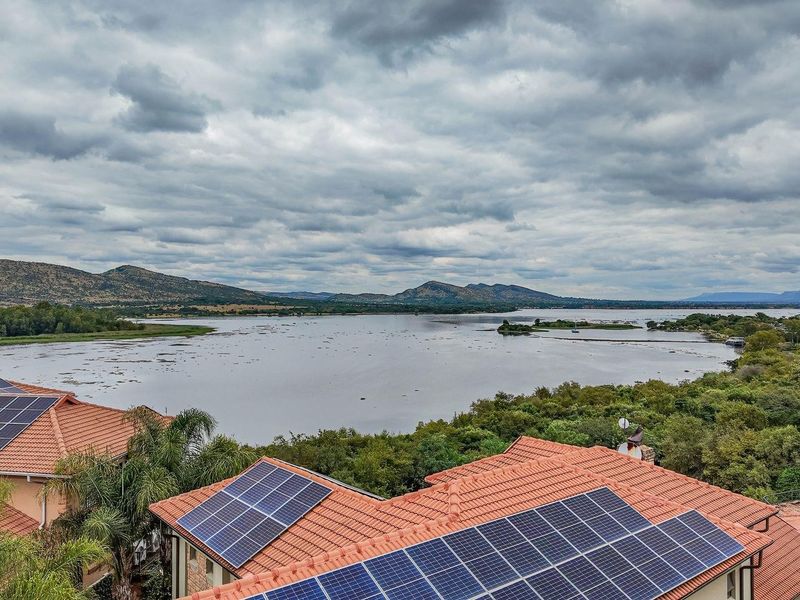 Aerial view of the property featuring multiple roof-mounted solar panel arrays overlooking a scenic lake and surrounding landscape.