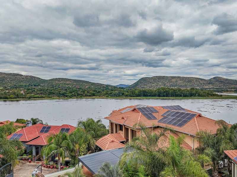Aerial view of residential properties featuring tiled roofs with integrated solar panel installations, overlooking a scenic lake and mountain landscape.