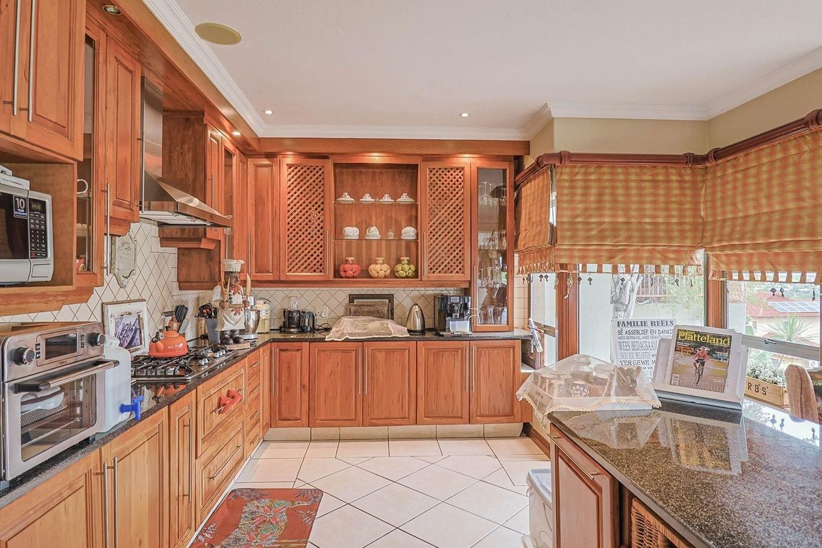 A traditional kitchen featuring warm wooden cabinetry, granite countertops, a gas hob, and tiled flooring, offering a functional and classic cooking space.