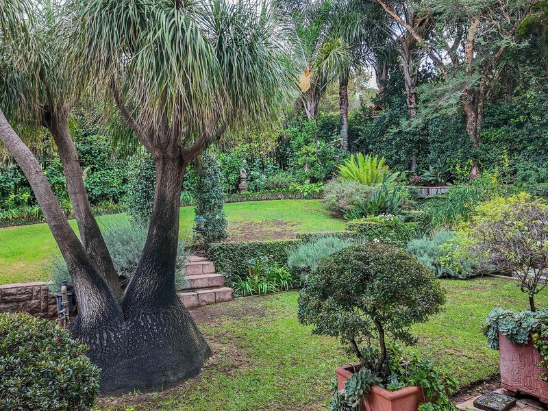 A lush, well-maintained garden featuring mature trees, manicured lawn, stone retaining walls, and stone steps, providing a serene outdoor environment.