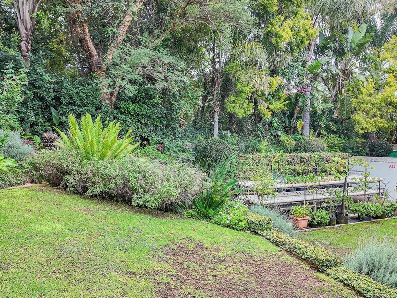 A lush, well-established garden featuring a manicured lawn, mature trees, and dense perimeter landscaping, providing a private and serene outdoor environment.