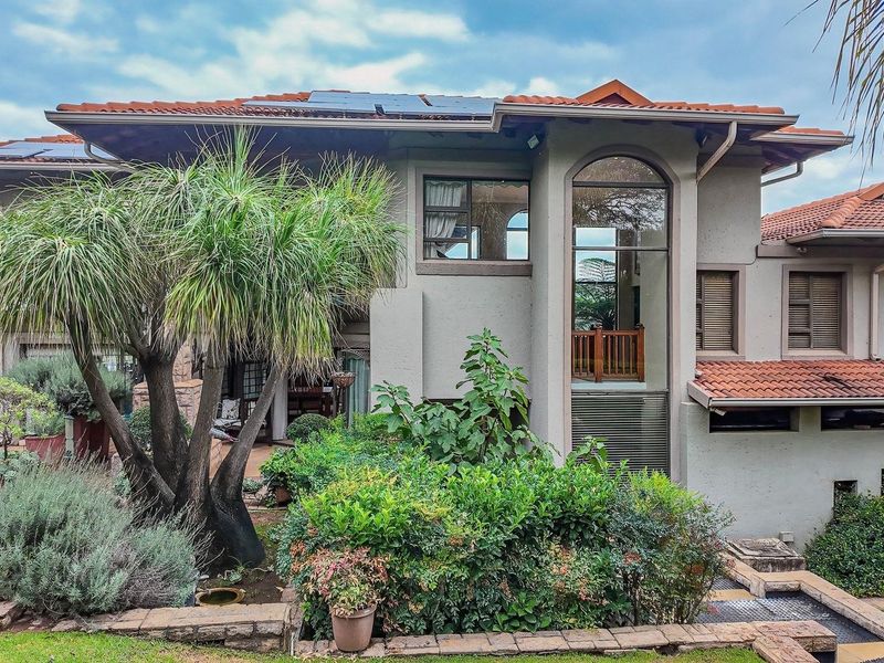 A well-maintained rear elevation of a multi-story house featuring terracotta roof tiles, solar panels, and an arched window overlooking a landscaped garden.