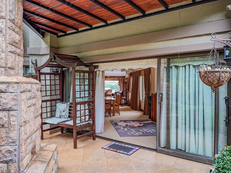 Covered patio area featuring stone cladding, timber pergola, and large sliding glass doors providing seamless access to the interior living space.