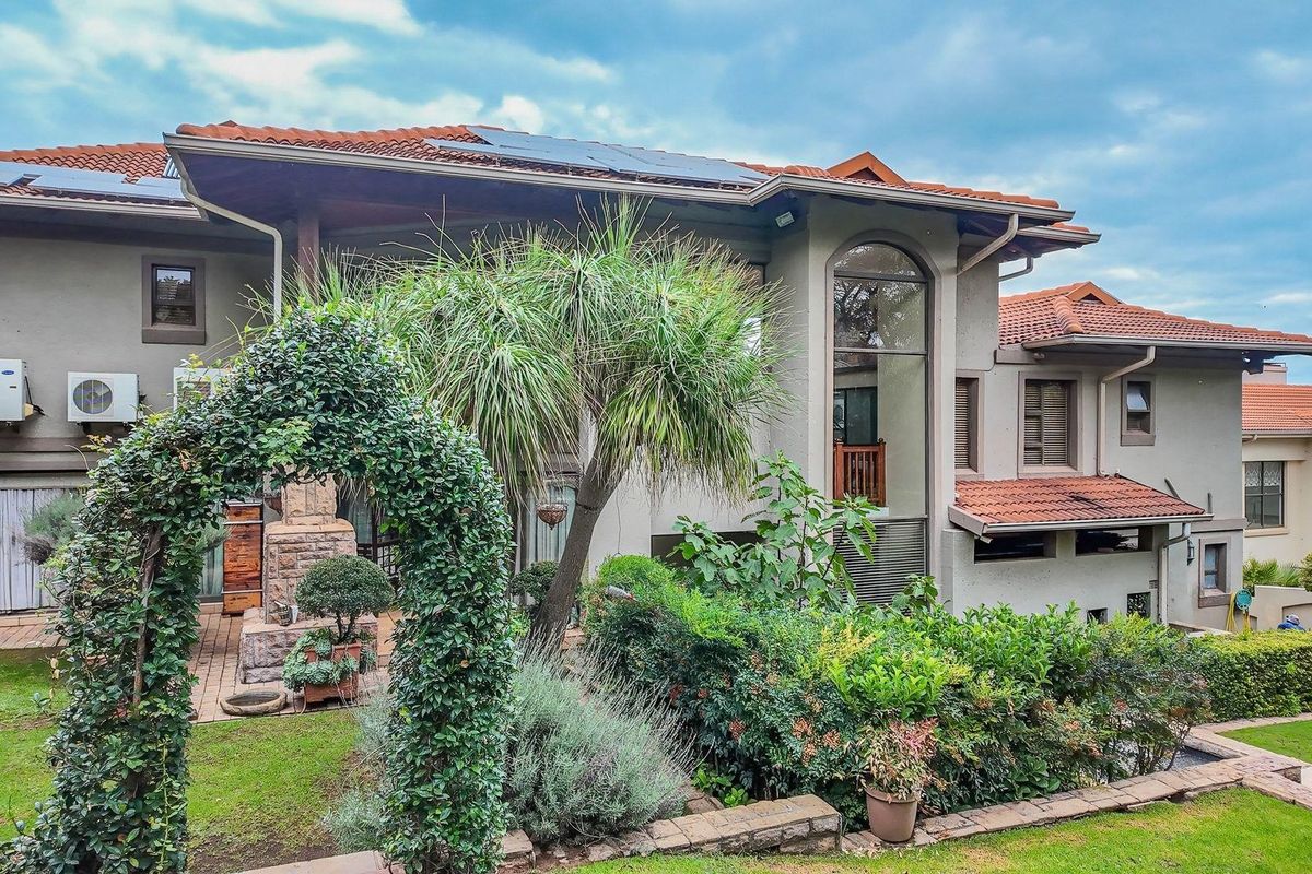 Rear view of a multi-story residence featuring terracotta roof tiles, solar panels, and a landscaped garden with a paved patio area.
