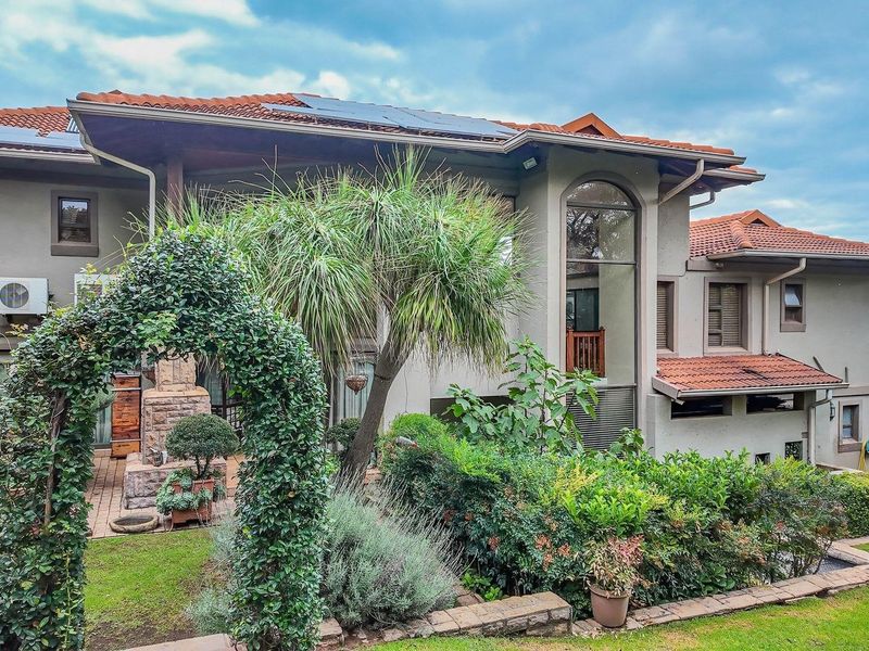 Rear view of a multi-story residence featuring terracotta roof tiles, solar panels, and a landscaped garden with a paved patio area.