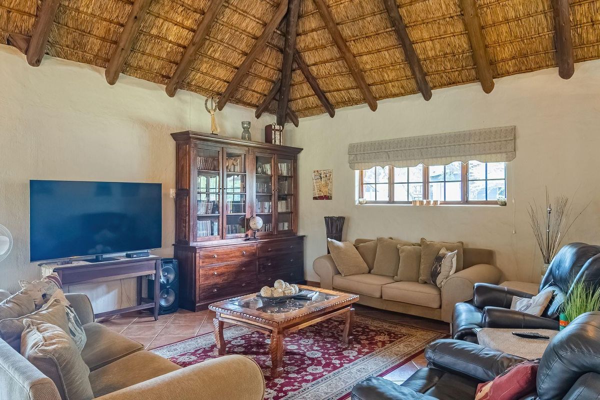 A cozy living room featuring a traditional high-pitched thatched roof with exposed timber beams and terracotta floor tiles.