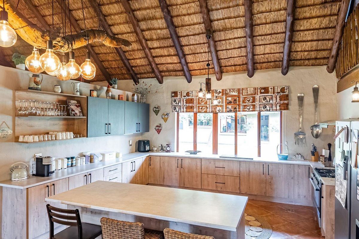 Spacious farmhouse kitchen featuring a high vaulted thatched ceiling with exposed timber beams, modern cabinetry, a central island, and large windows.