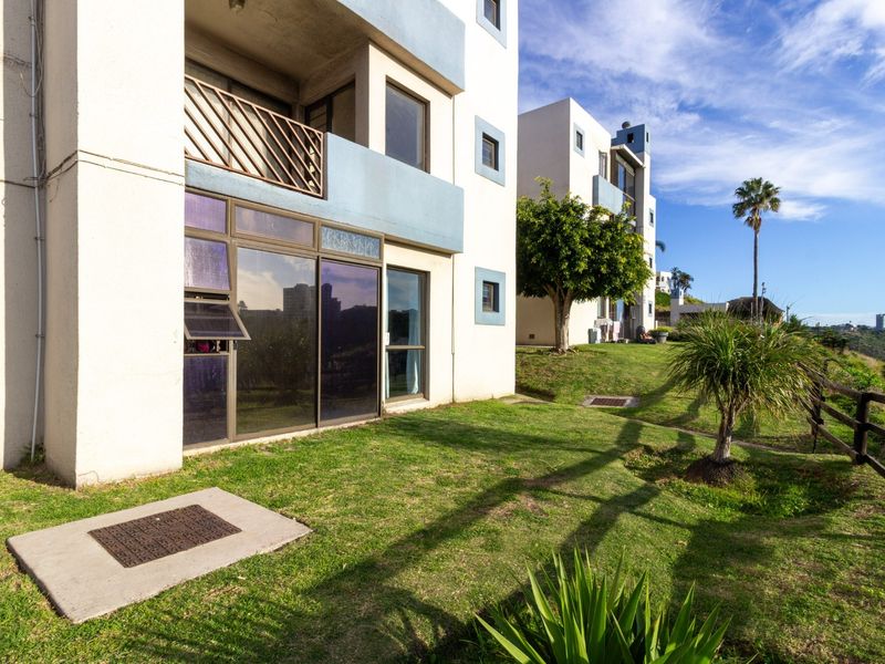 Rear view of the apartment building featuring a ground-floor patio with sliding glass doors, a balcony above, and a well-maintained communal garden area.