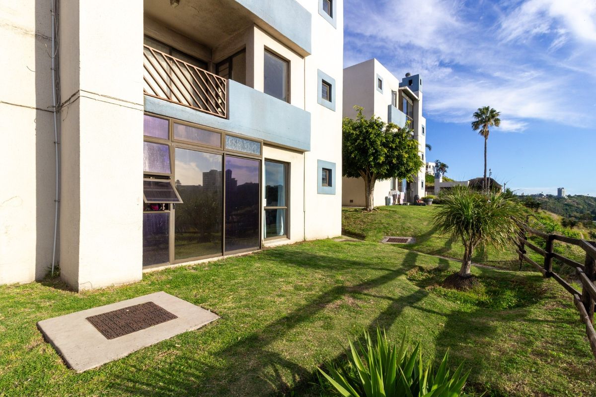 Rear view of the apartment building featuring a ground-floor patio with sliding glass doors, a balcony above, and a well-maintained communal garden area.