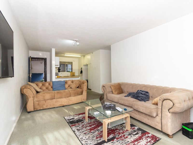 Open plan living area featuring carpeted flooring and a functional kitchen space with built-in cabinetry and sink.