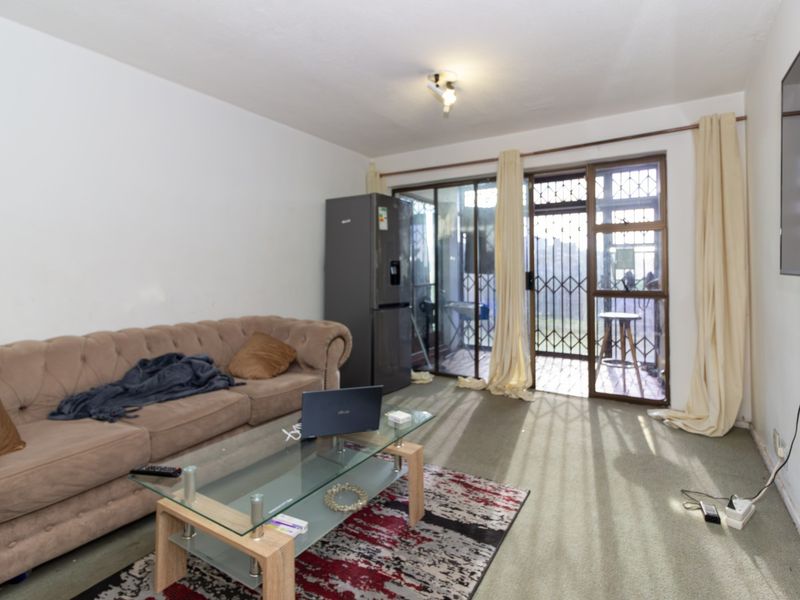 Living room featuring carpet flooring, a ceiling light fixture, and a sliding glass door with an integrated security gate leading to the patio.
