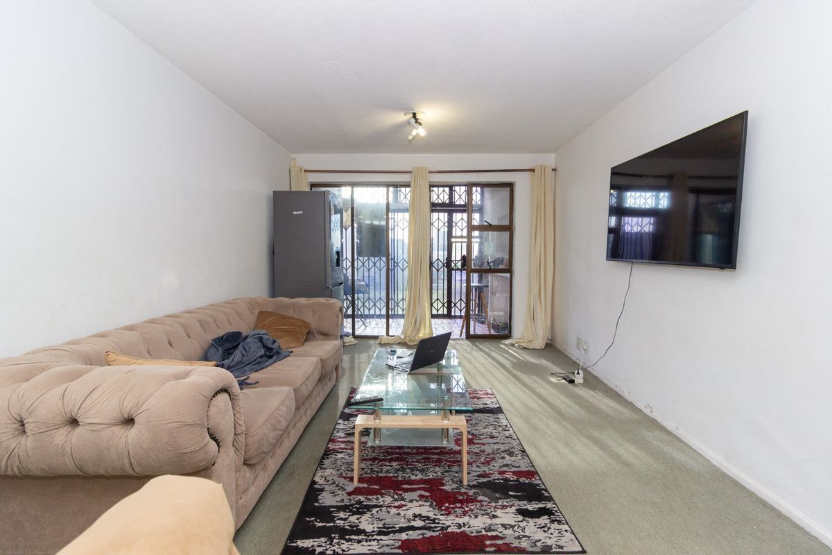 A living room featuring carpeted flooring and a sliding glass door with security gate leading to an outdoor area.
