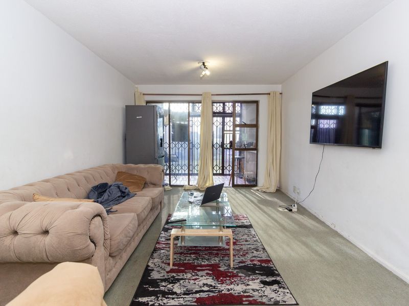 A living room featuring carpeted flooring and a sliding glass door with security gate leading to an outdoor area.