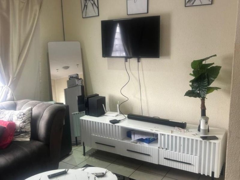 A living room area featuring tiled flooring and a wall-mounted television setup.