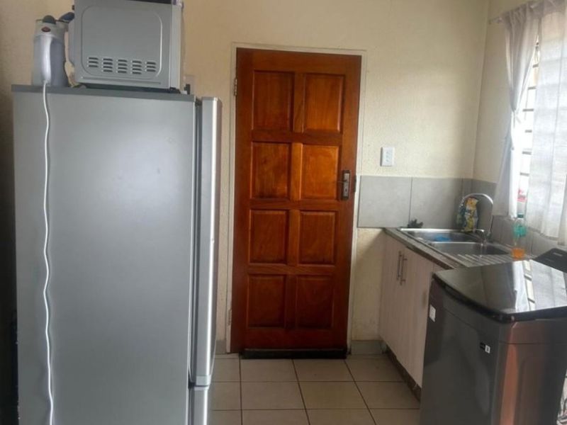 A functional laundry area featuring tiled flooring, a stainless steel sink, built-in cabinetry, and a solid timber door.