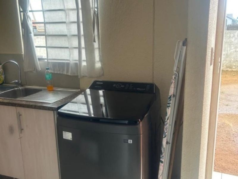 A functional laundry area featuring a stainless steel sink, built-in cabinetry, and tiled flooring with direct access to the exterior.