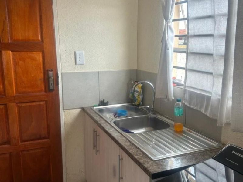 A functional laundry area featuring a stainless steel sink, laminate countertop, built-in cabinetry, and tiled flooring with direct access to an exterior door.