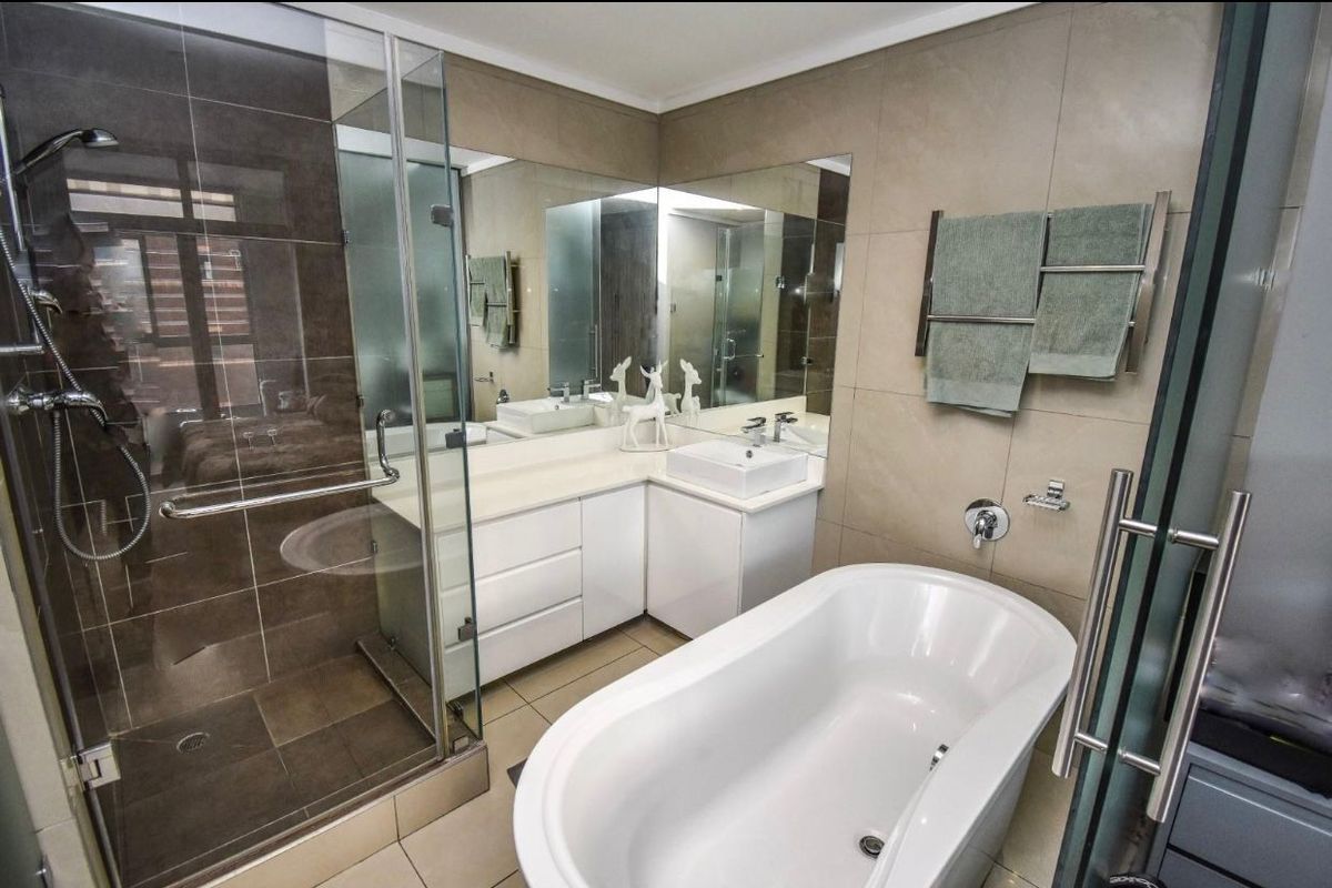 Modern bathroom featuring a freestanding bathtub, glass-enclosed shower, vanity with basin, and large wall-mounted mirror.