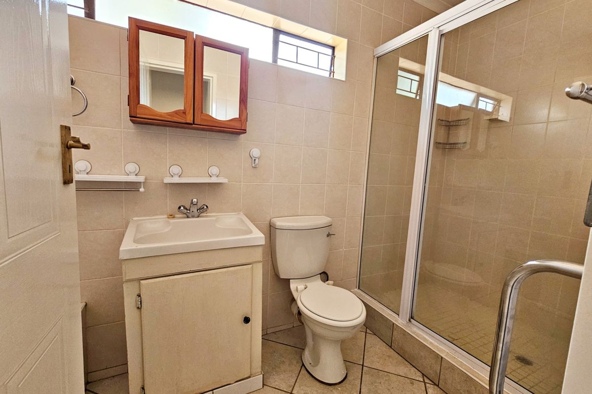 A functional bathroom featuring a shower enclosure, vanity cabinet with basin, toilet, and neutral wall tiling with high-level windows for natural light.