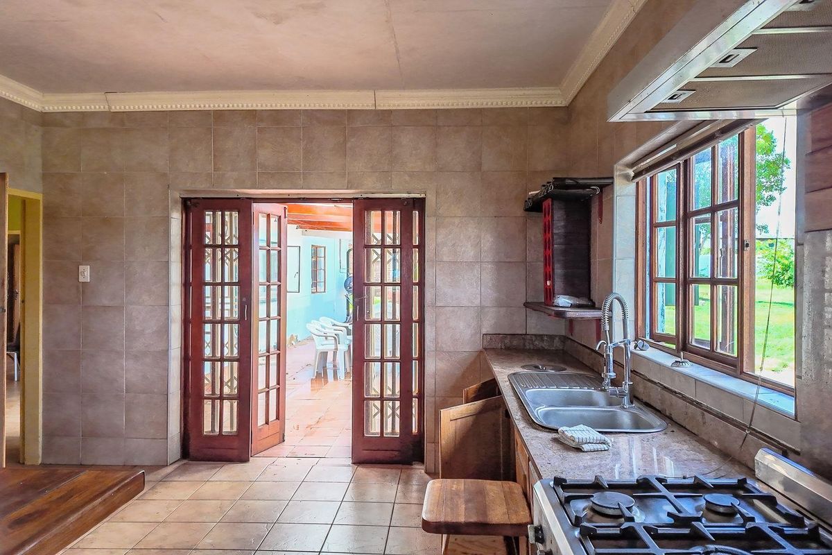 A functional kitchen featuring granite countertops, a gas hob, and double sink, with direct access through wooden french doors to an outdoor patio area.