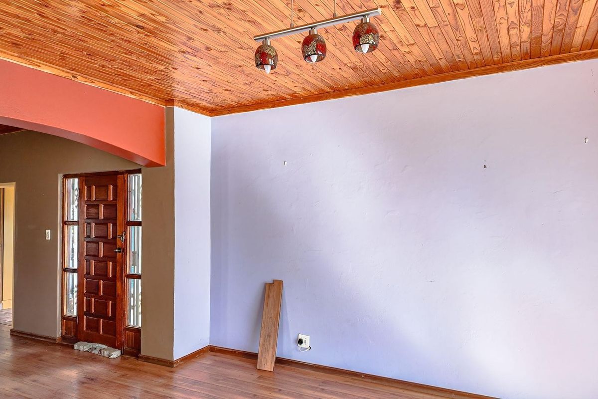 An empty living room featuring a timber ceiling, laminate flooring, and a wooden entrance door with glass panels.
