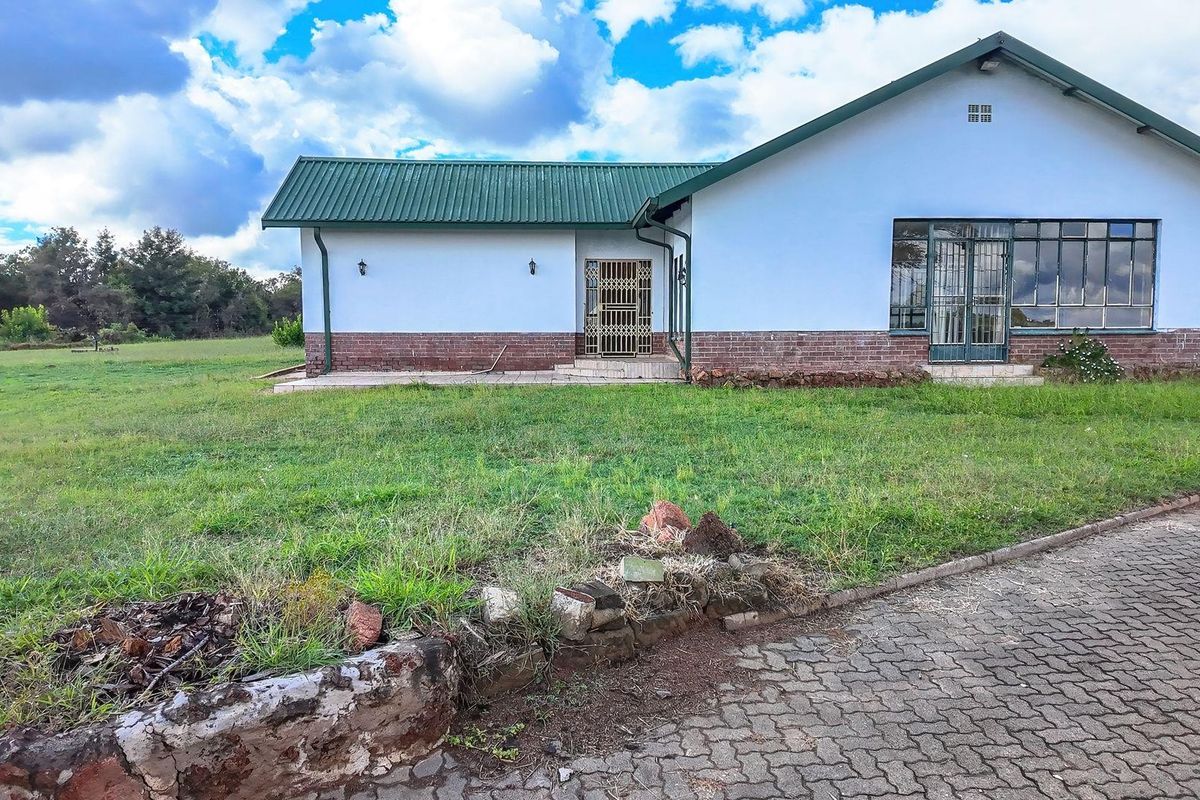 Rear view of a farm-style residence featuring a corrugated metal roof, brick base detailing, and a paved driveway area.