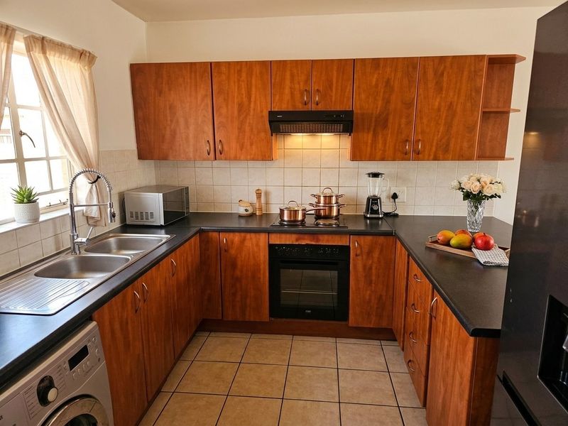 A functional U-shaped kitchen featuring wood-look cabinetry, dark countertops, built-in oven, hob, extractor fan, and tiled flooring with ample storage space.