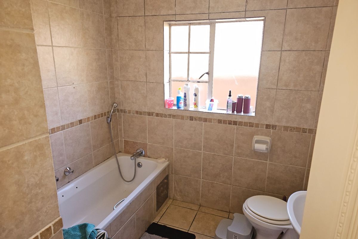A functional bathroom featuring tiled walls and flooring, a bathtub with a handheld shower mixer, and a standard toilet.