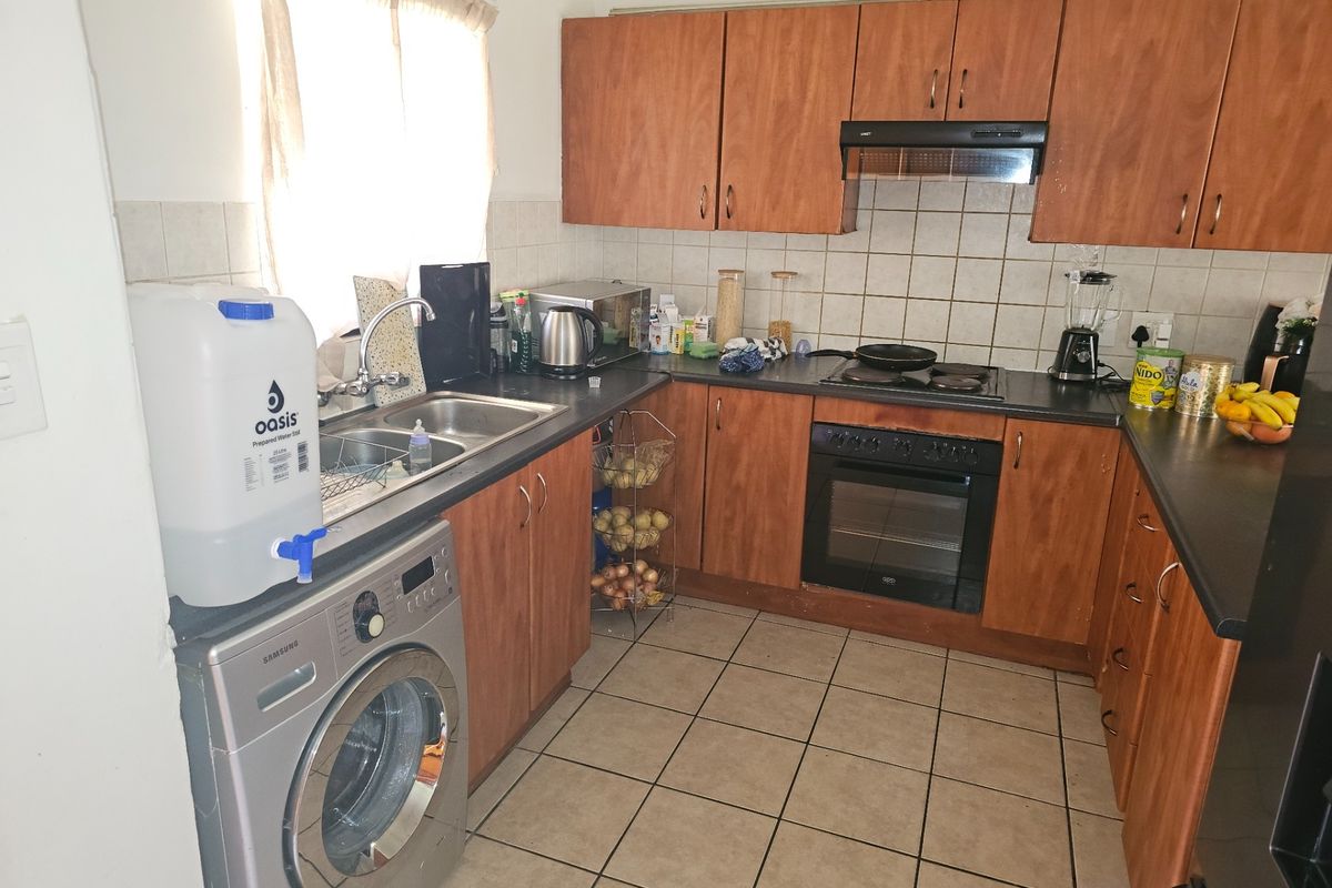 Functional kitchen featuring wood-look cabinetry, built-in oven with hob, extractor fan, and tiled flooring, offering a practical layout for daily meal preparation.