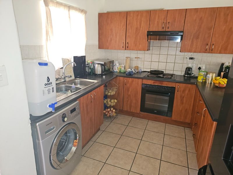 Functional kitchen featuring wood-look cabinetry, built-in oven with hob, extractor fan, and tiled flooring, offering a practical layout for daily meal preparation.