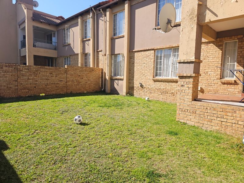 Rear view of a multi-story apartment complex featuring a private lawn, brick facade, and a covered patio area.