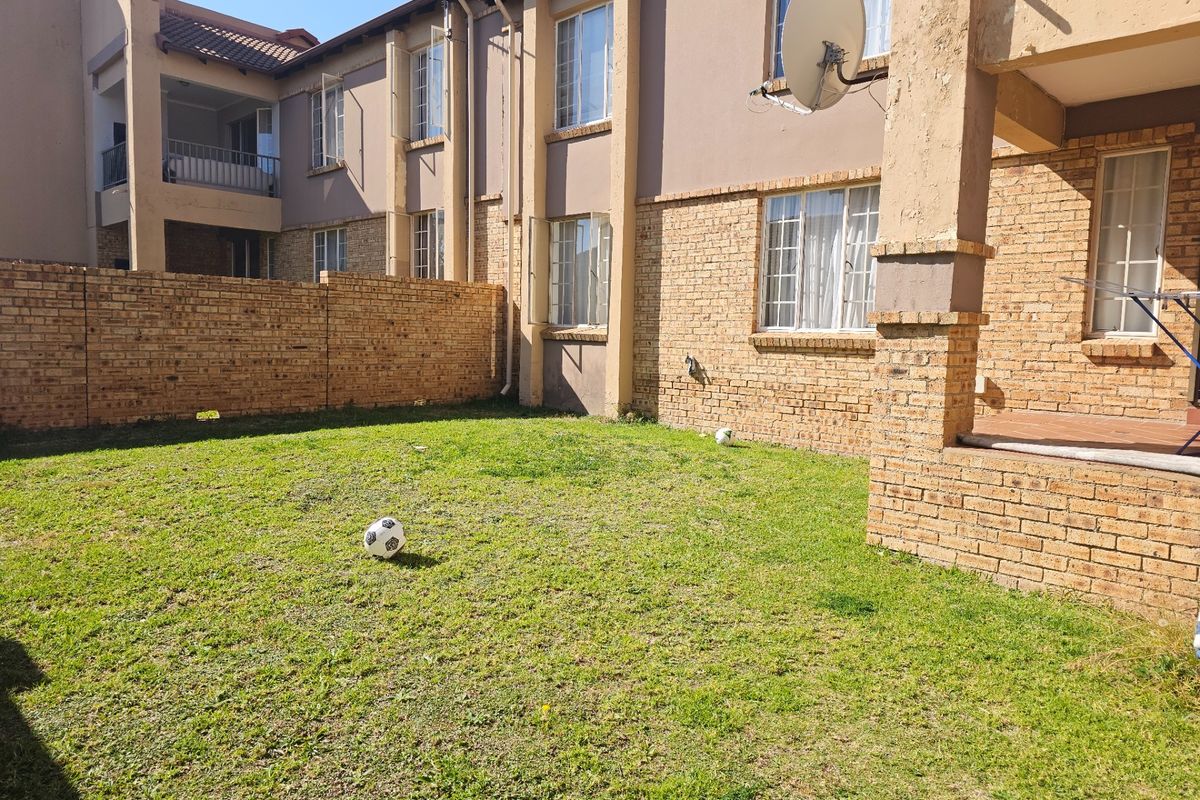 Rear view of a multi-story apartment complex featuring a private lawn, brick facade, and a covered patio area.