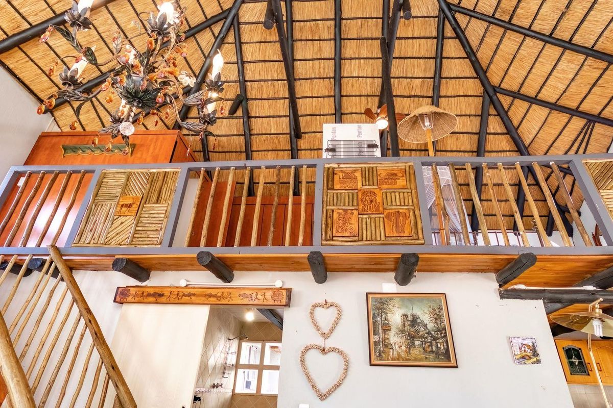 A rustic interior space featuring a high vaulted thatched roof with exposed timber beams and a mezzanine level with decorative wooden railings.