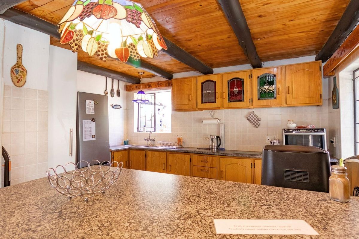 A rustic kitchen featuring wooden cabinetry, exposed timber ceiling beams, tiled splashbacks, and a granite-topped breakfast bar.