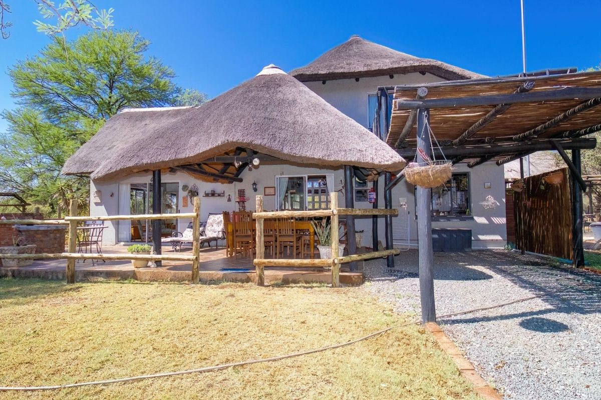 Rear view of a farm-style residence featuring a thatched roof, covered patio area, and rustic timber fencing set within a natural garden landscape.