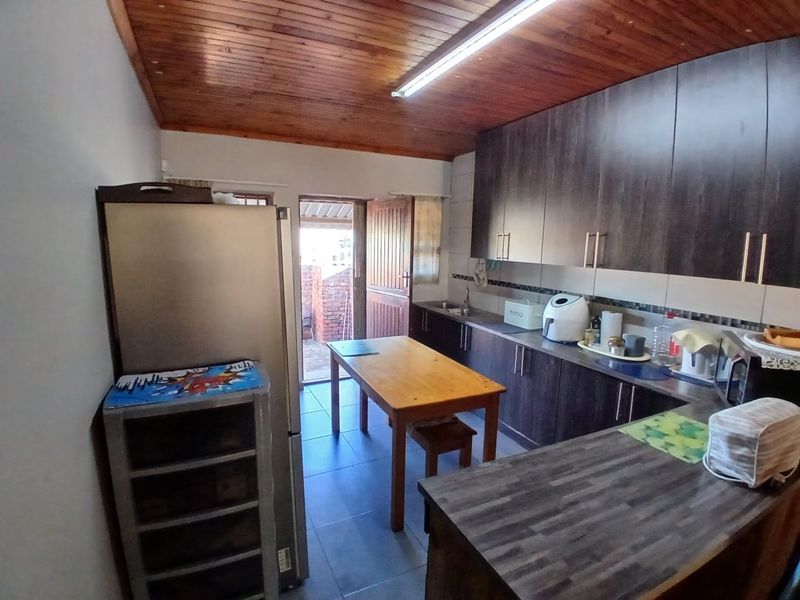 A functional kitchen featuring dark wood-look cabinetry, laminate countertops, tiled flooring, and a distinctive timber-paneled ceiling with direct access to an outdoor area.