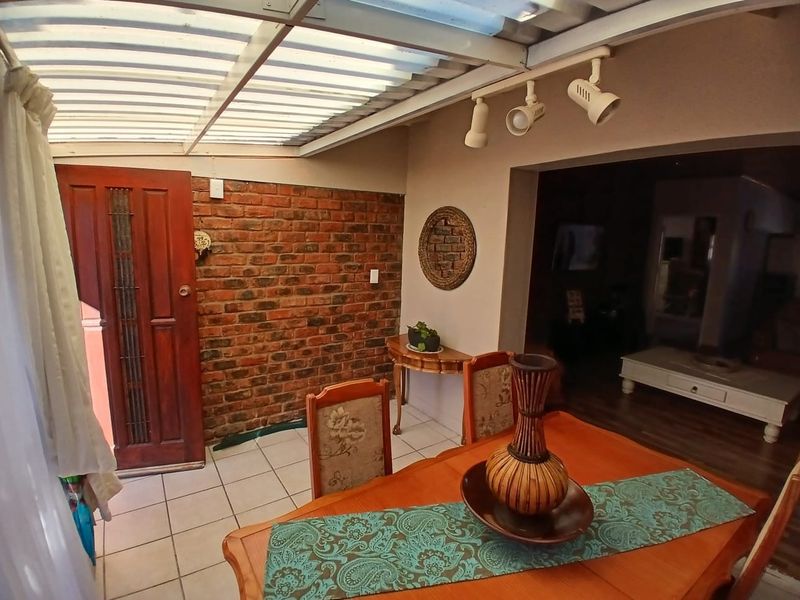 A covered patio area featuring a brick accent wall, tiled flooring, and adjustable track lighting, providing a transition space to the interior living area.