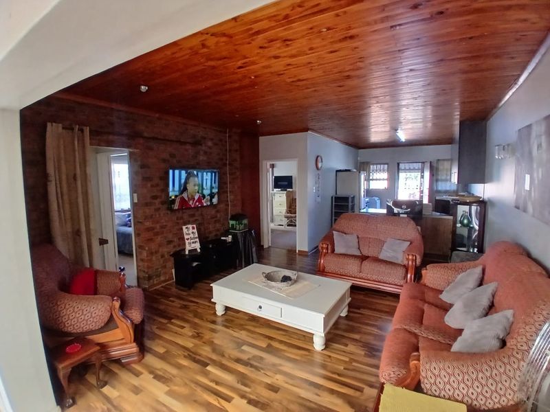 Spacious open-plan living area featuring a rustic brick accent wall, timber-clad ceiling, and durable wood-look flooring, providing a warm and inviting atmosphere.