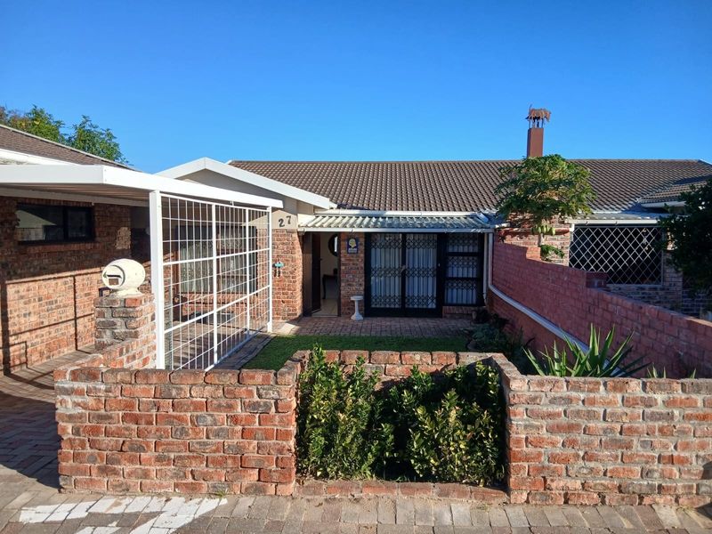 Front elevation of a townhouse featuring a face-brick facade, paved courtyard, covered carport, and secure metal entrance gates.