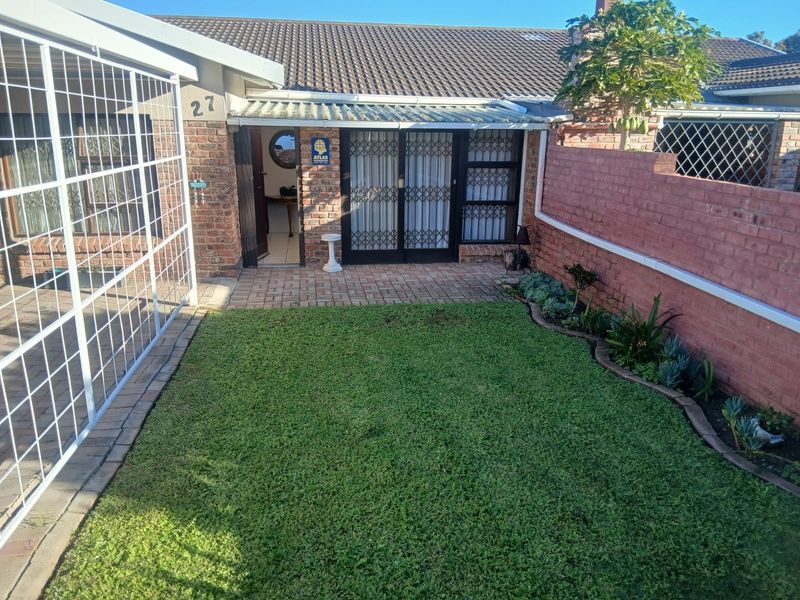 A private rear courtyard featuring a paved patio area, a small lawn, and a brick boundary wall with established garden beds.